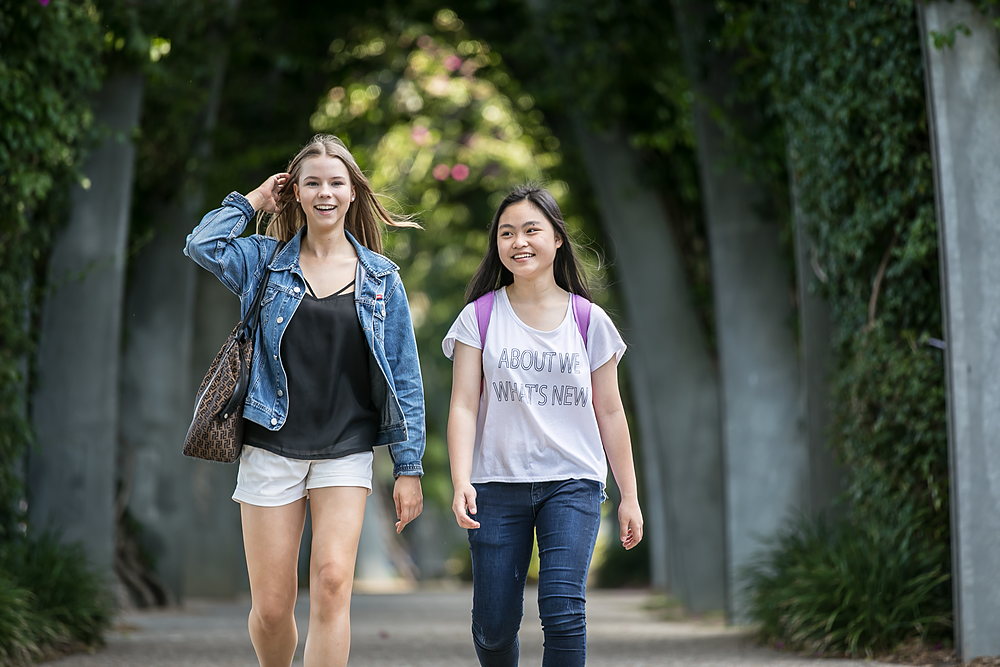 Two students walking and laughing together along a shaded garden path in the Brisbane South Bank parklands