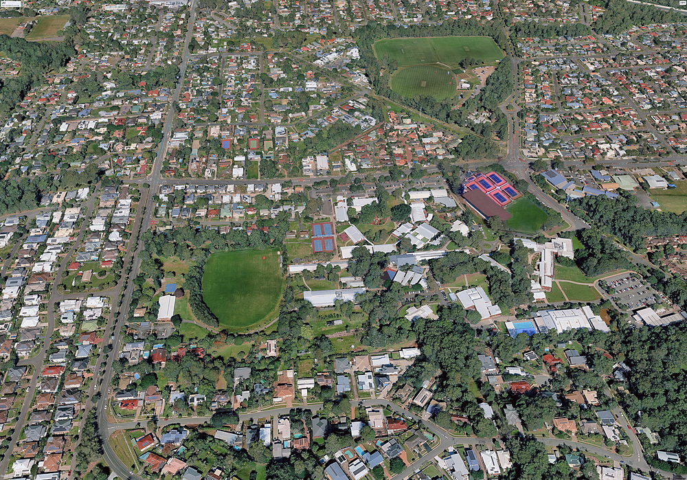 Aerial view of the John Paul College campus at Daisy Hill — playing fields, courts and buildings set among trees, with the College grounds outlined in gold