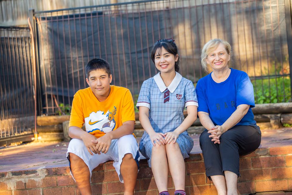 A host mother sitting outside in the afternoon sun with her homestay student and her son