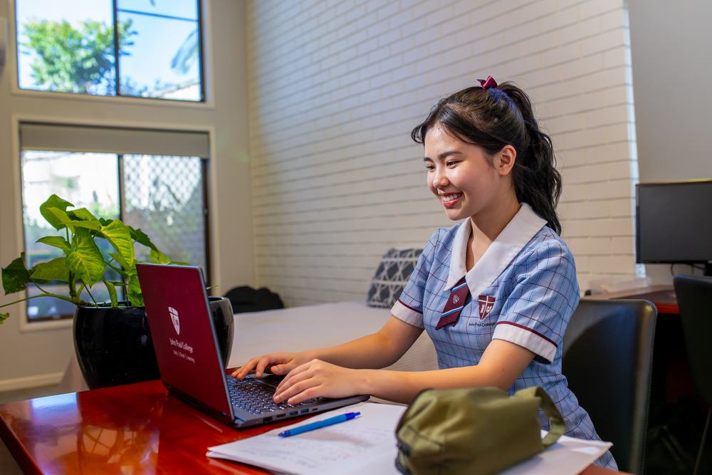 A homestay student smiling while doing her homework on a laptop