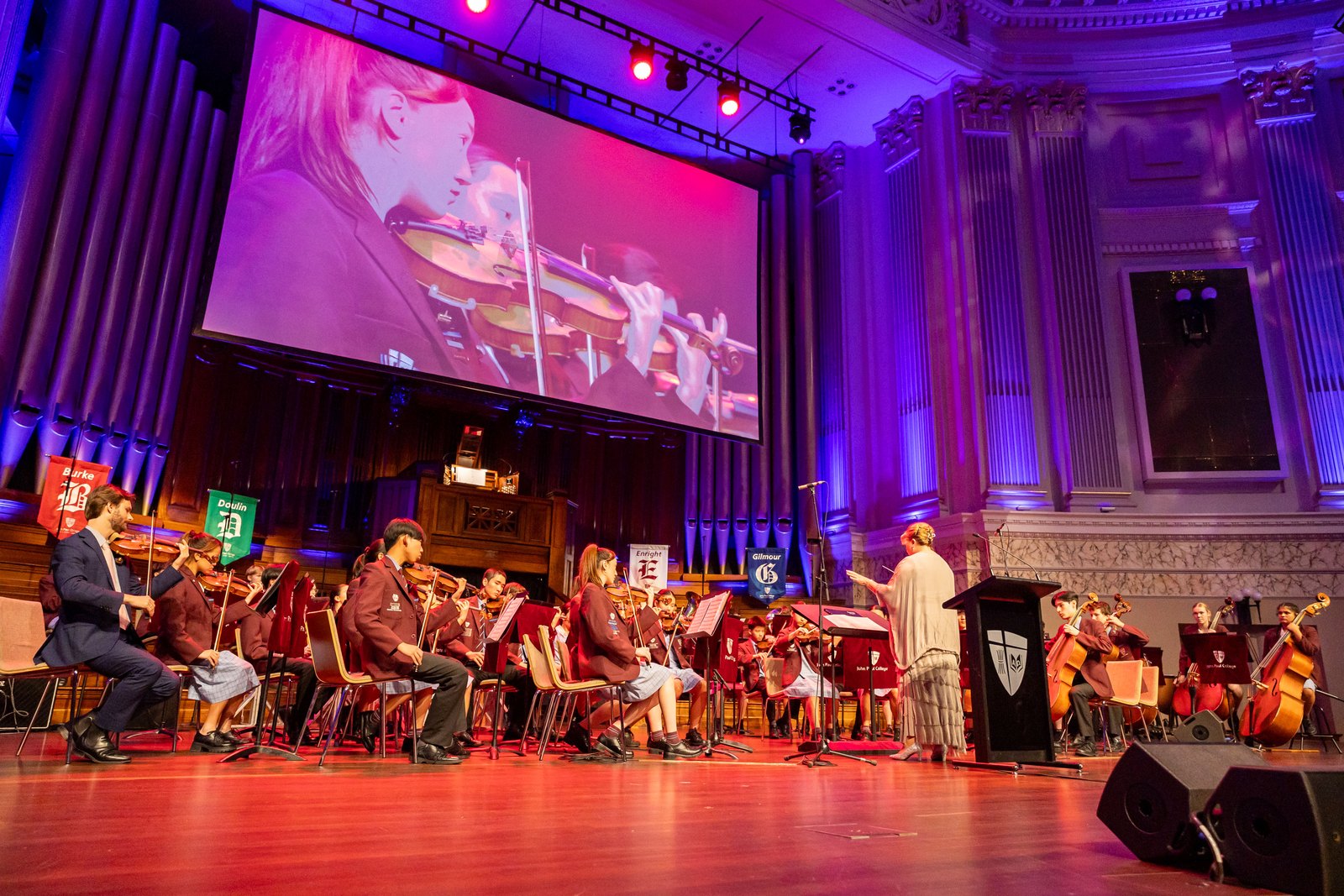 The John Paul College orchestra performing on stage in a grand concert hall