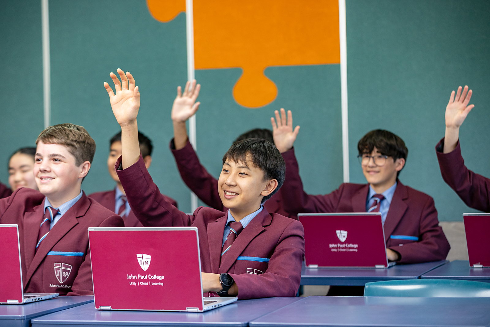 Students raising their hands in a mainstream class at John Paul College