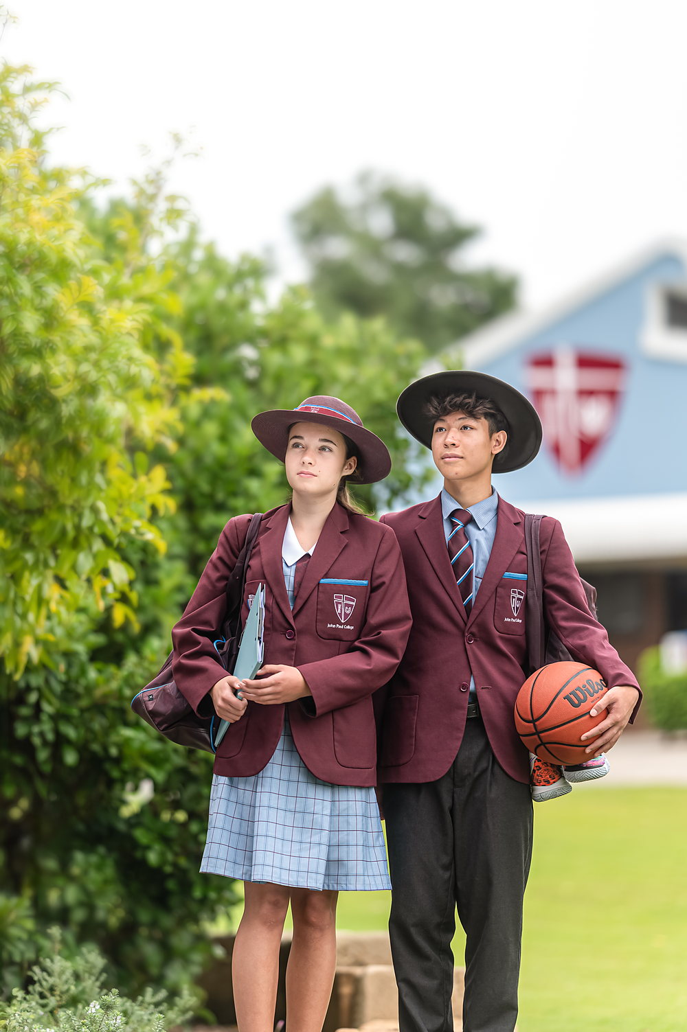 Two John Paul College students walking out of class at the end of the day, one carrying a basketball