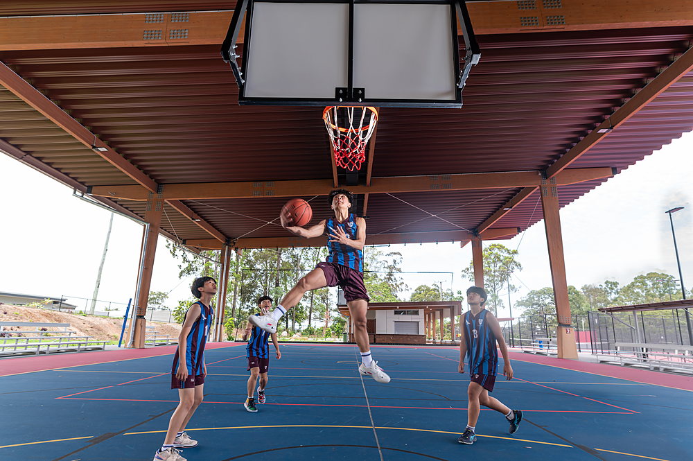 Estudiantes de John Paul College jugando un partido informal de básquetbol en la cancha exterior cubierta a la hora de almuerzo