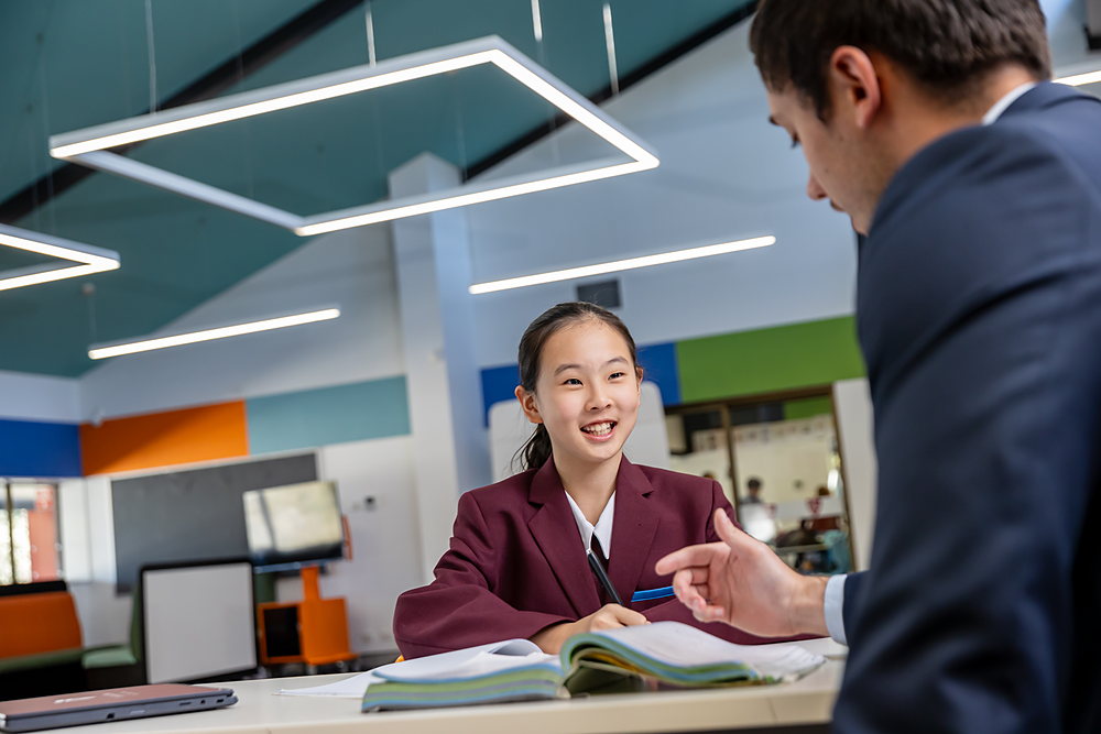 A JPC teacher leaning in to help an international student with her work in class