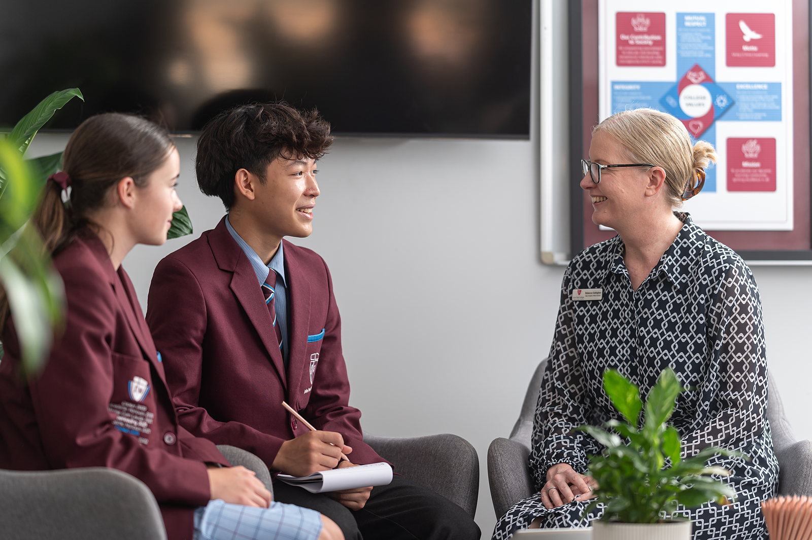 Two John Paul College students in uniform talking with a smiling member of the international student support team