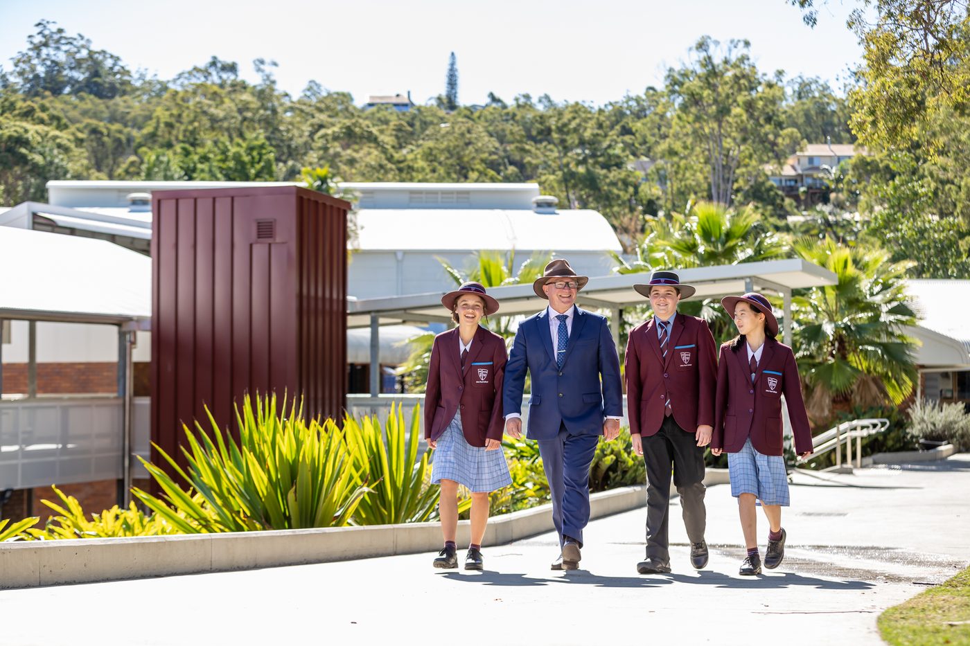 A John Paul College teacher walking through the sunny campus with three happy international students in uniform